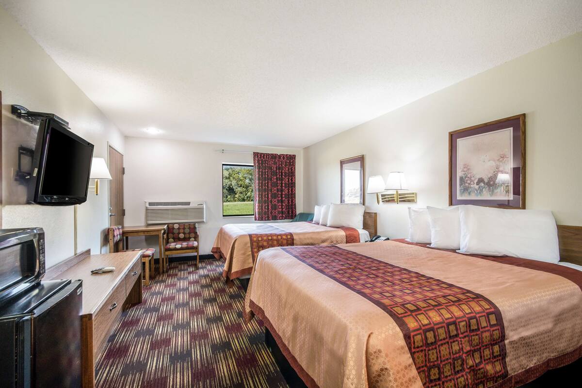 A hotel room with two beds, a desk with a TV, a chair, and a window with curtains.
