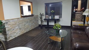 A modern living room with a stone accent wall, a glass coffee table, a leather sofa, and a potted plant. - Americas Best Value Inn & Suites Harrisonville (Harrisonville)