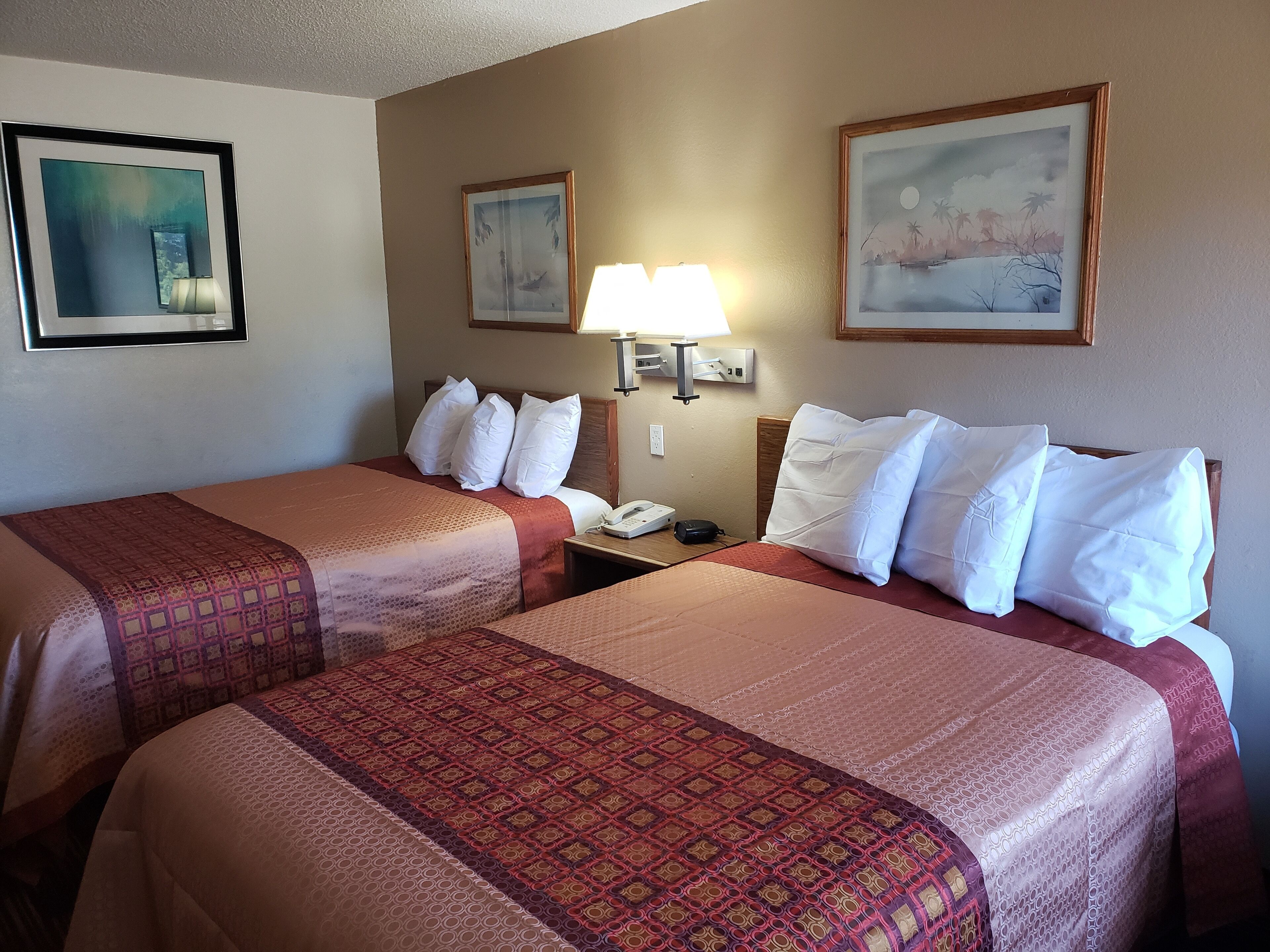 A hotel room with two beds, each with a patterned bedspread, a nightstand with a lamp, and two framed pictures on the wall.