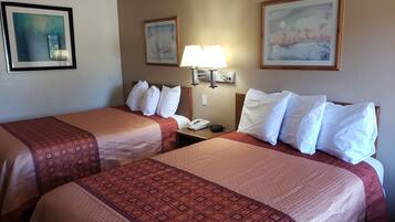 A hotel room with two beds, each with a patterned bedspread, a nightstand with a lamp, and two framed pictures on the wall.