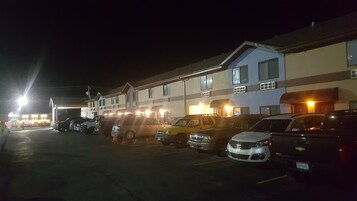 Un estacionamiento con varios coches aparcados frente a un edificio de techos planos y numerosas ventanas.