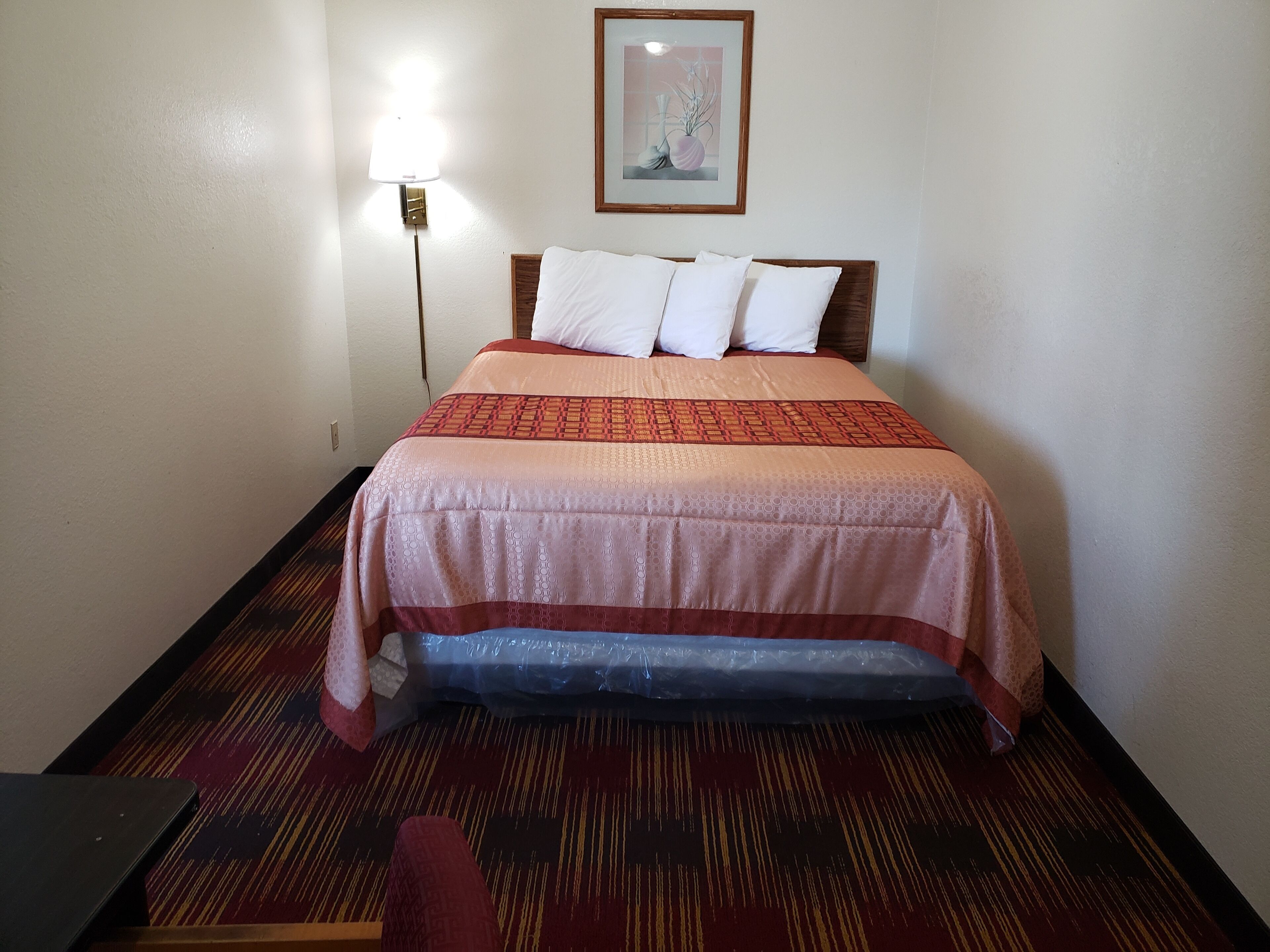 A hotel room with a bed, a nightstand, a lamp, and a framed picture on the wall.