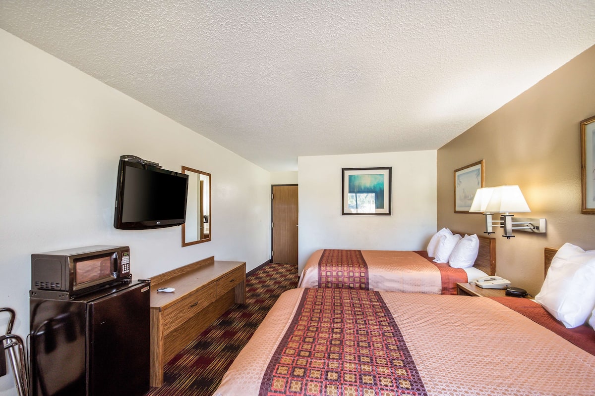 A hotel room with two beds, a TV, a microwave, a dresser, and a desk.
