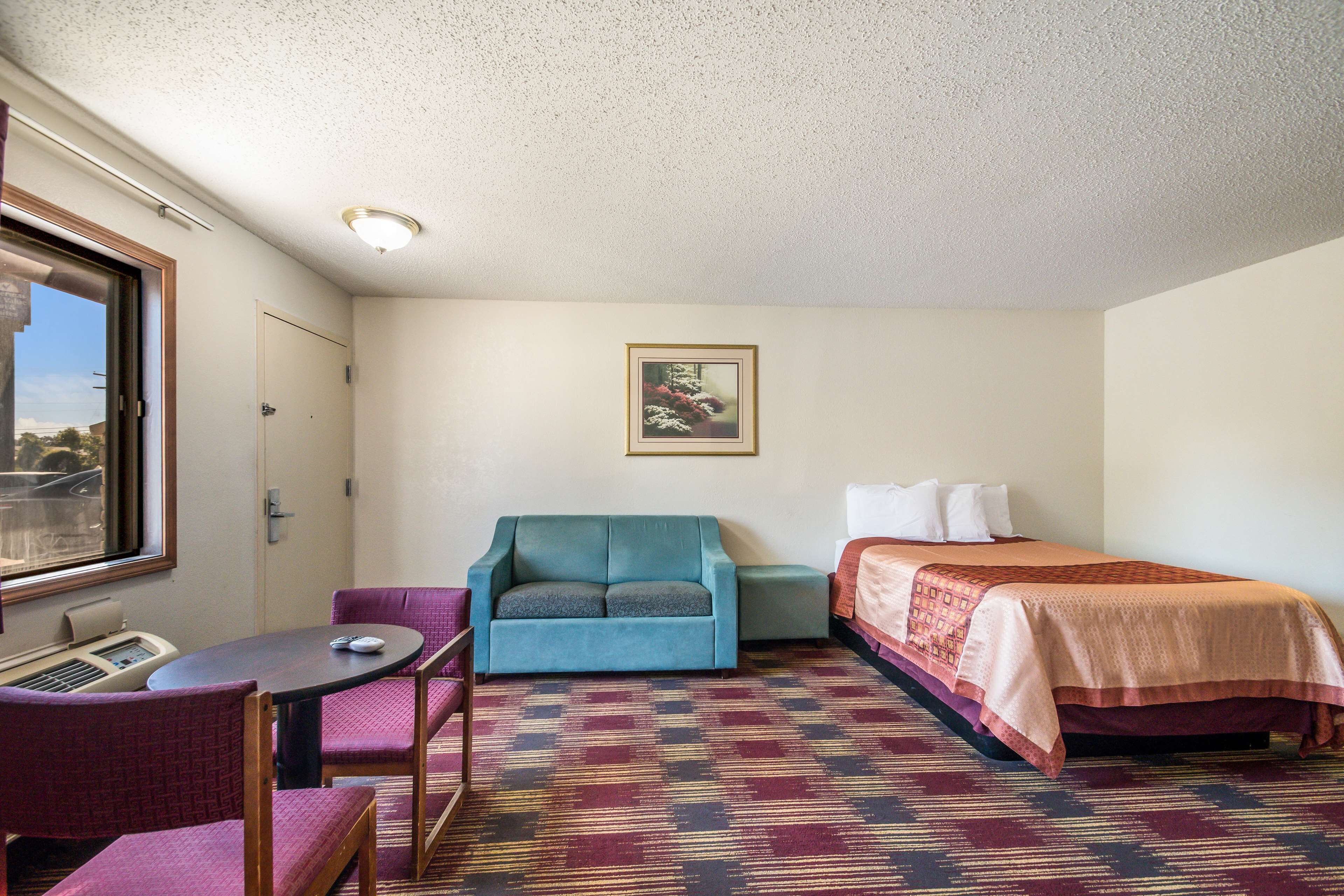 Une petite chambre d’hôtel avec un lit simple, un canapé, une chaise, une petite table et une fenêtre.