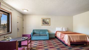 Une petite chambre d’hôtel avec un lit simple, un canapé, une chaise, une petite table et une fenêtre.