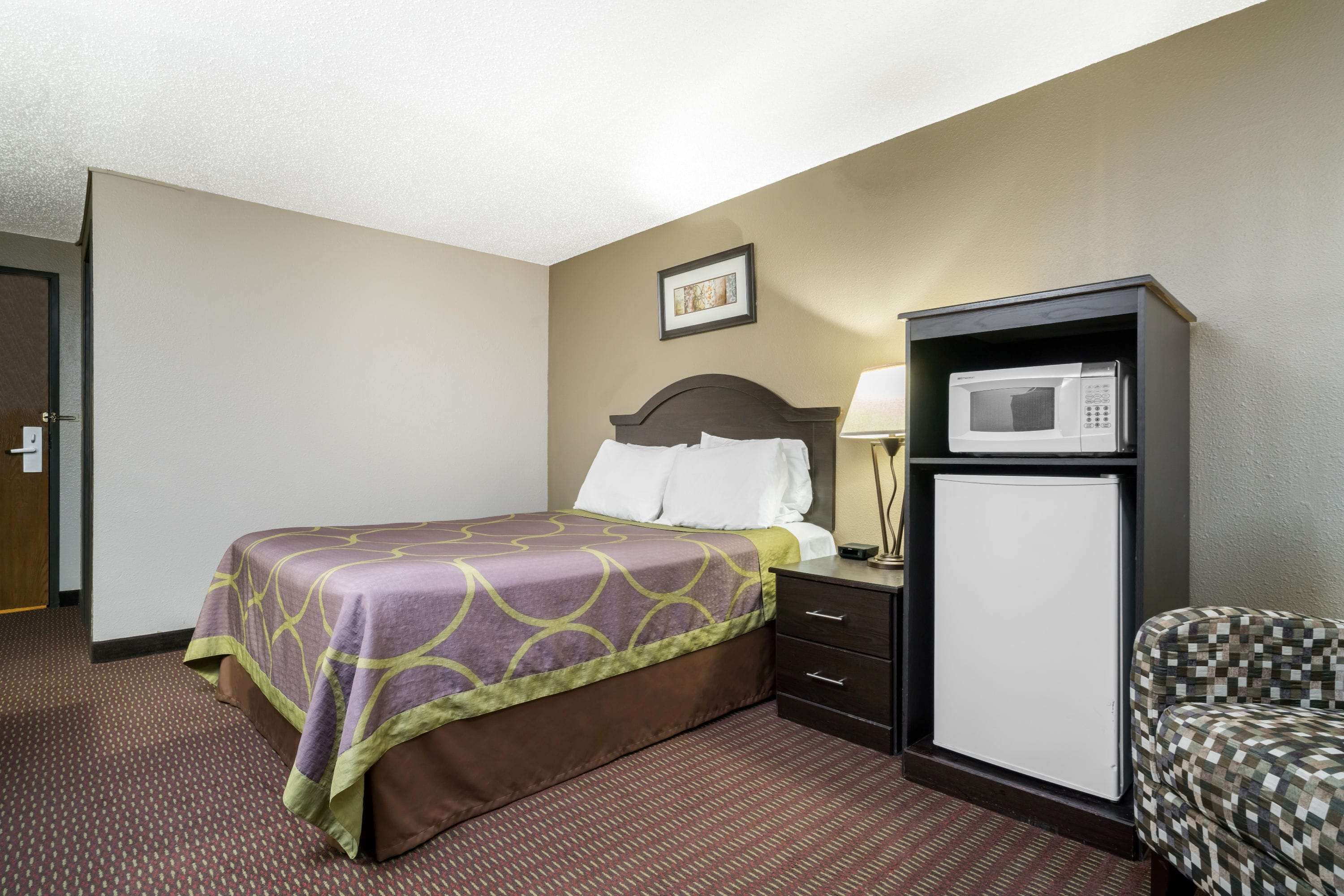 Une chambre d’hôtel avec un lit, un bureau doté d’un micro-ondes, une chaise et une porte.