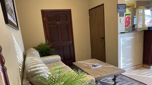 Um hall com sofá, mesa de centro, porta e geladeira.
