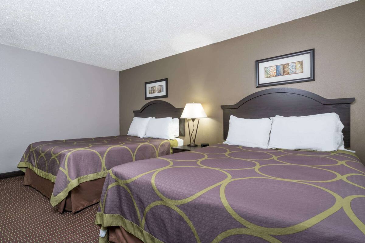 A hotel room with two beds, each with a headboard, a bedside table with a lamp, and framed artwork on the wall.