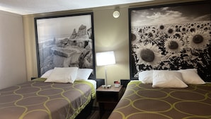 Quarto de hotel com duas camas, uma mesinha de cabeceira, uma luminária e uma parede com um mural com tema de natureza.
