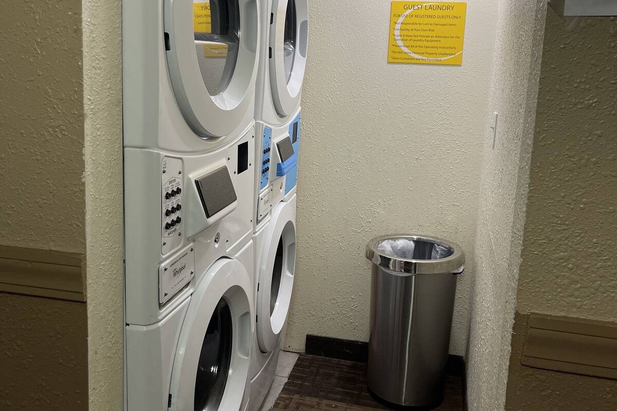 A laundry area with stacked washers and dryers, a trash bin, and a sign indicating guest laundry use.