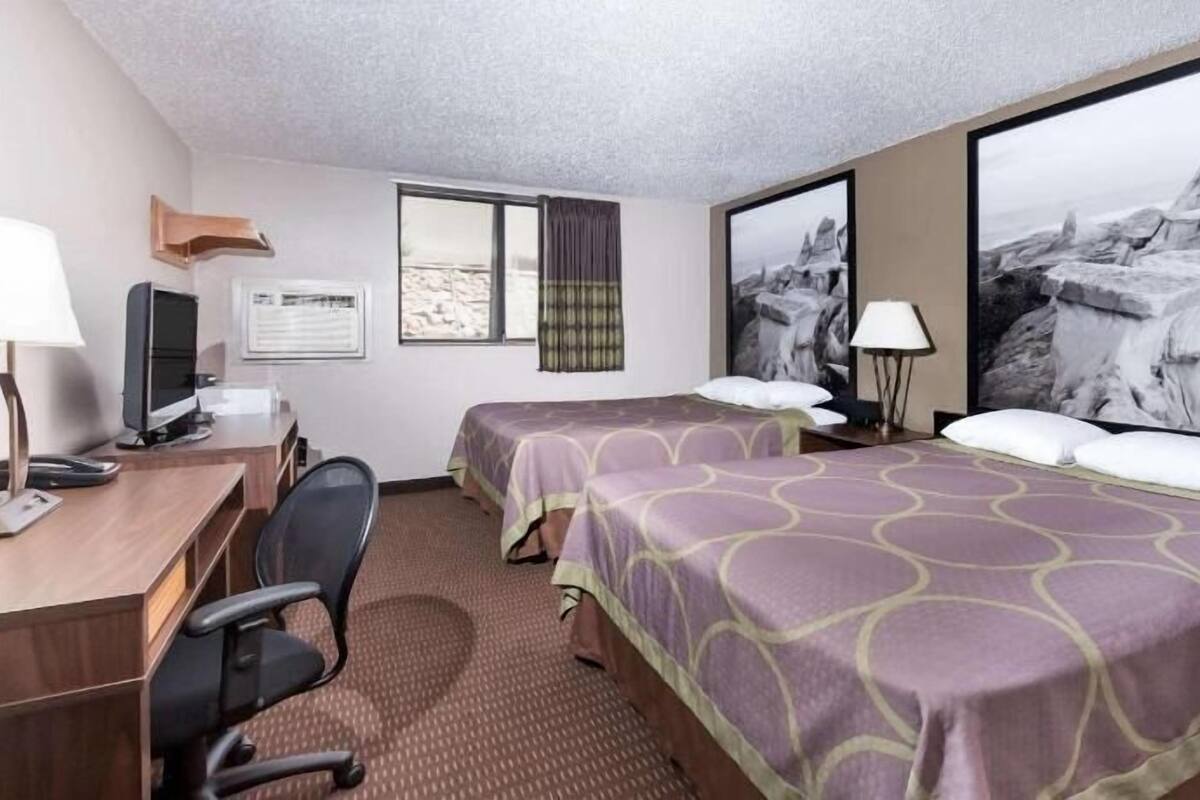 A hotel room with two beds, a desk with a computer, a chair, and large windows.