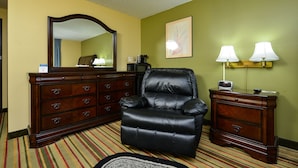 Habitación de hotel con un espejo grande, un sillón de cuero negro, un aparador de madera y dos lámparas de pared.