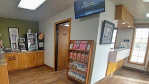Zona de recepción con mostrador de madera, una máquina de café y un televisor de pared mostrando tarifas.
