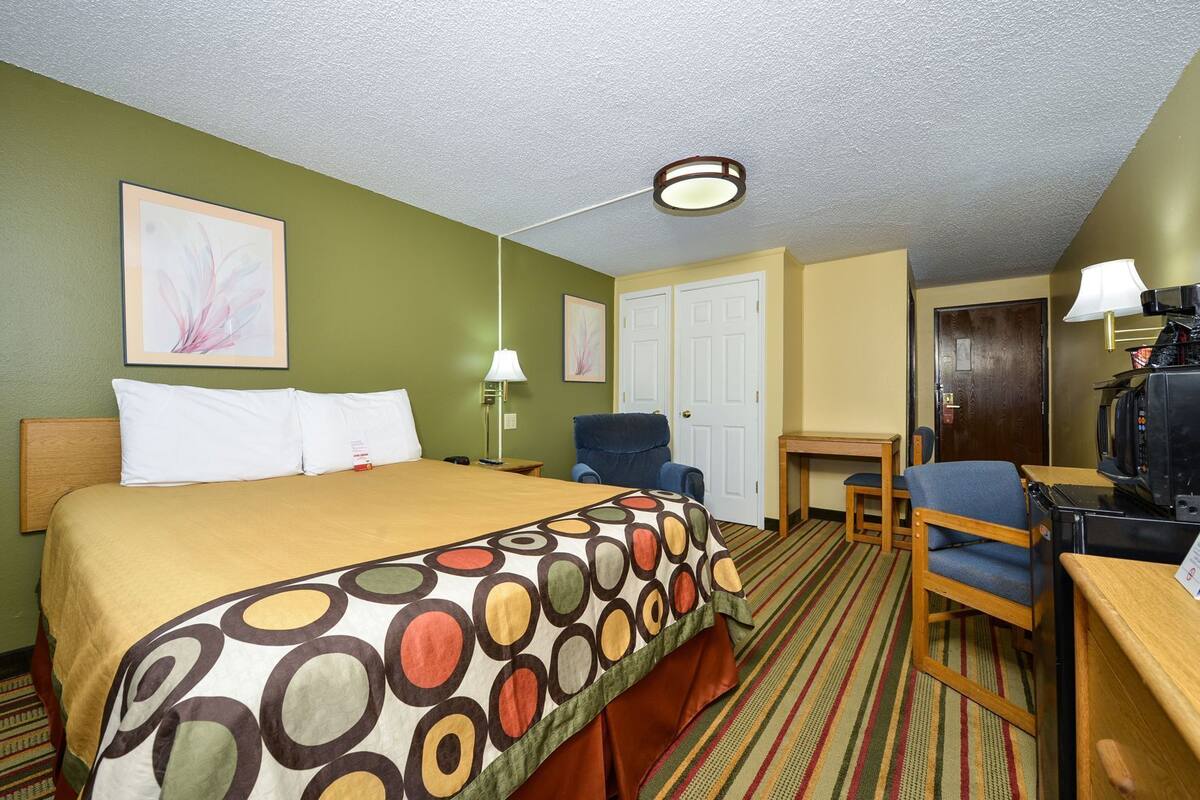 Una habitación de hotel con cama, escritorio, silla, televisor y puerta.