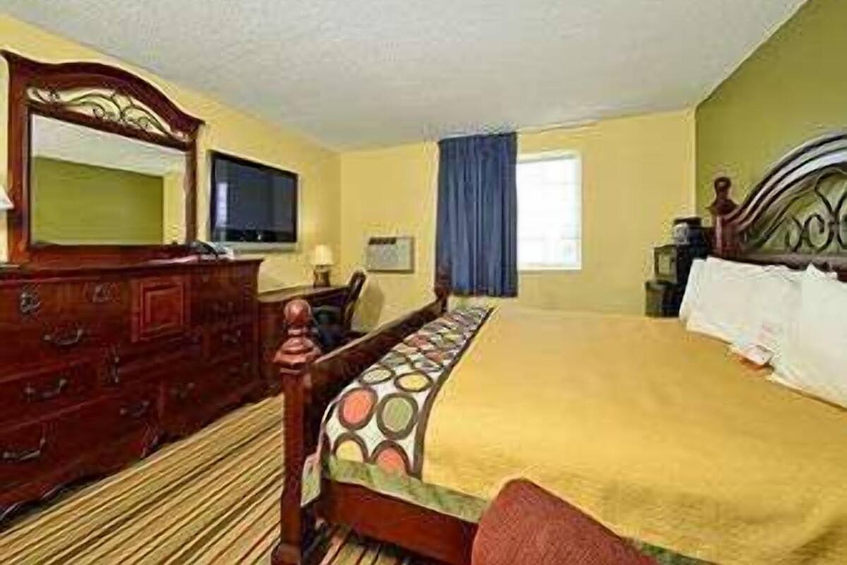 Una habitación de hotel con una cama de madera, un aparador, un televisor y una ventana con cortinas.