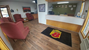 Un área de recepción con mostrador, un sillón rojo y piso de madera.