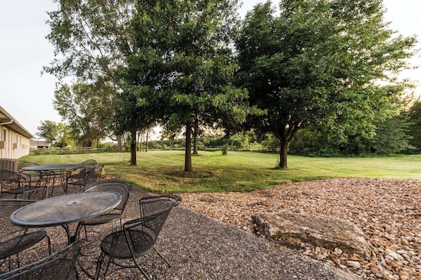 An outdoor patio with metal tables and chairs, surrounded by a gravel area and trees.