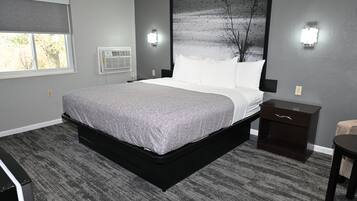 A modern bedroom with a large bed, a nightstand, a dresser, and a window with a view of trees.