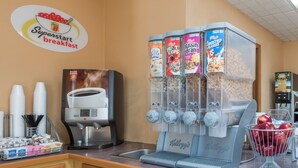 Una estación de desayuno con una máquina de café, varios dispensadores de cereales y un bol de fruta.
