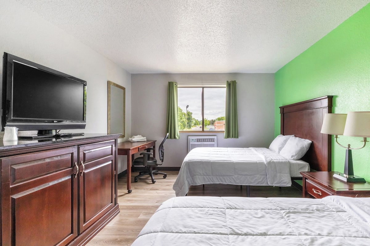 A hotel room with a bed, a desk with a chair, a television, and a window with curtains.
