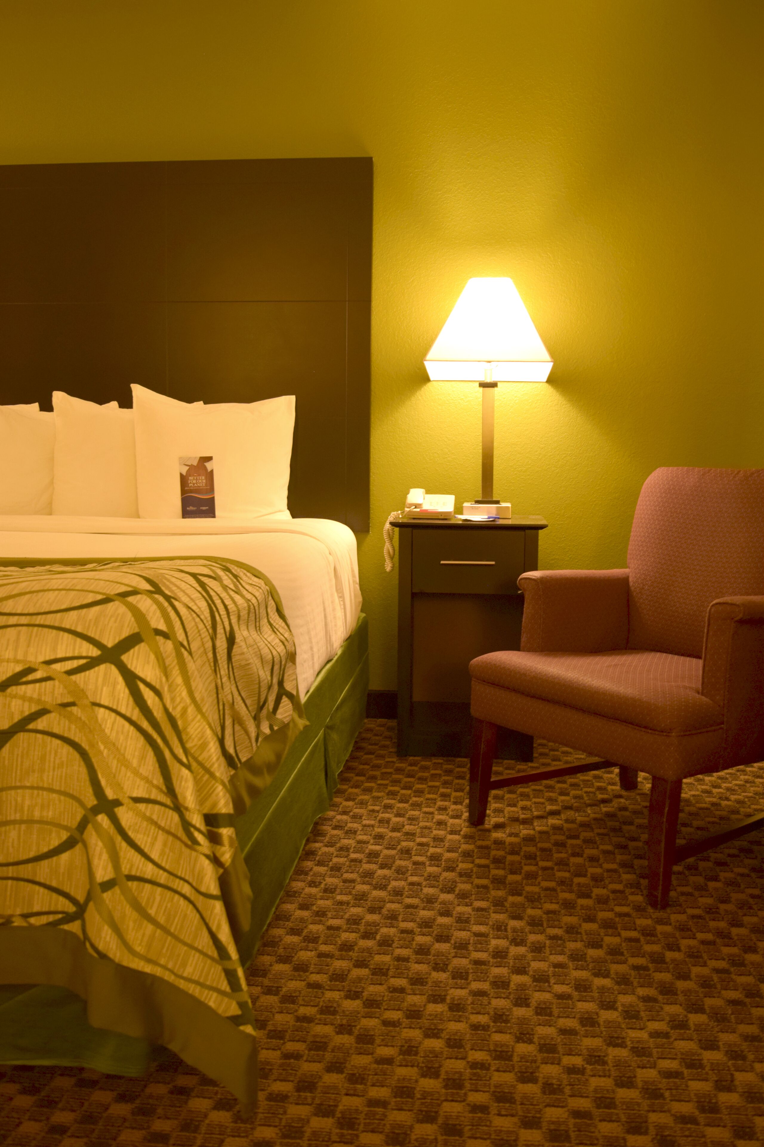 A hotel room with a bed, a nightstand, a lamp, and a chair.