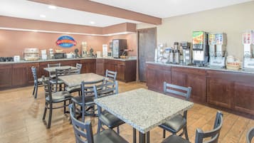 Un comedor con mesas y sillas, una cafetera y un refrigerador.