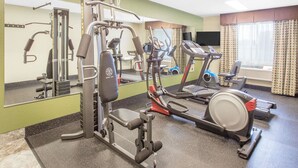 Een fitnessruimte met cardioapparatuur, gewichthefapparatuur en een spiegel.