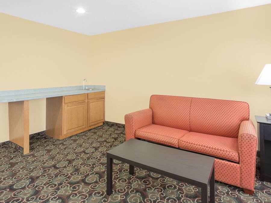 A room with a patterned carpet, a sofa, a coffee table, a desk with a sink, and a lamp.