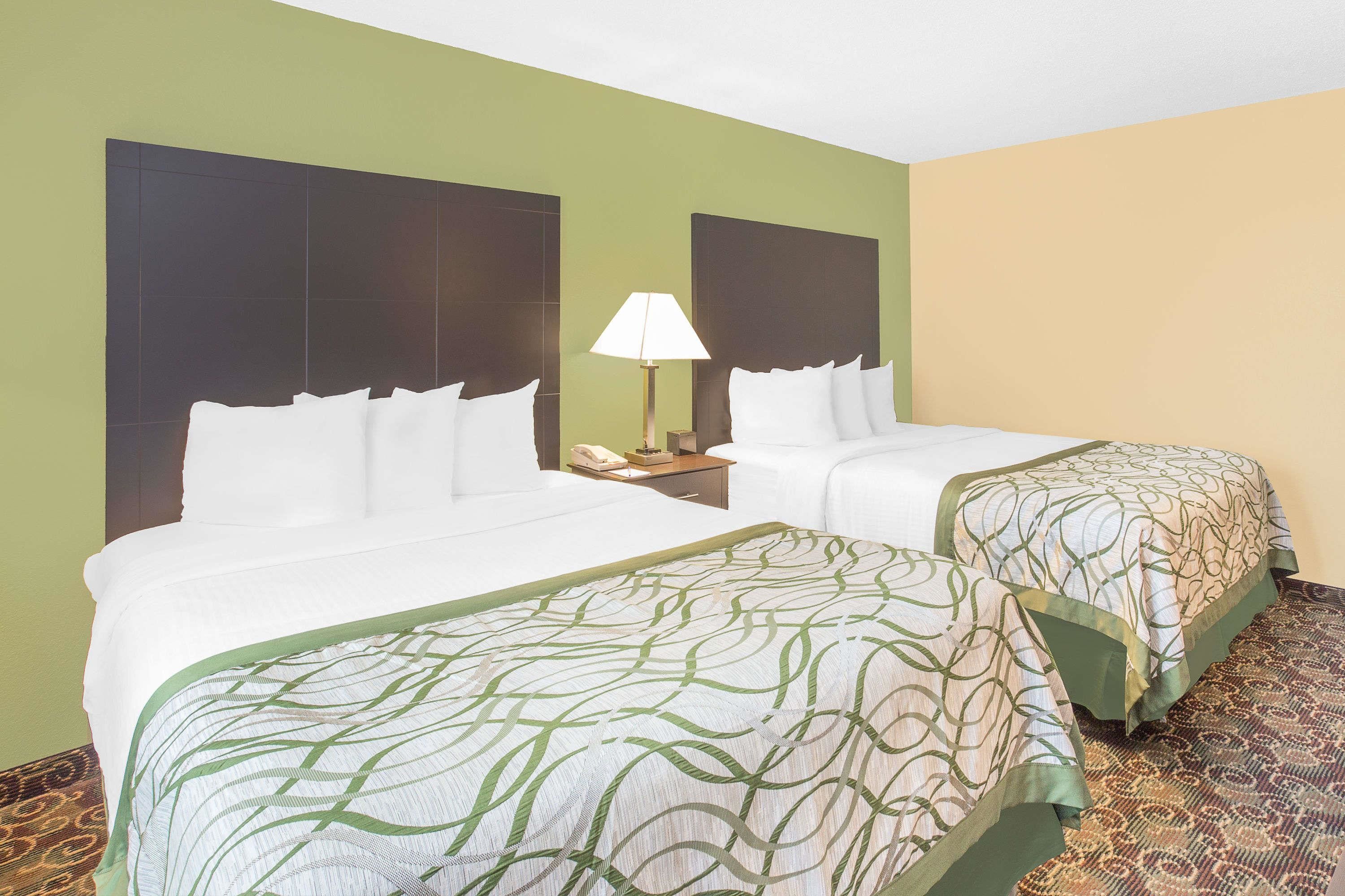 A hotel room with two beds, a nightstand, and a lamp.