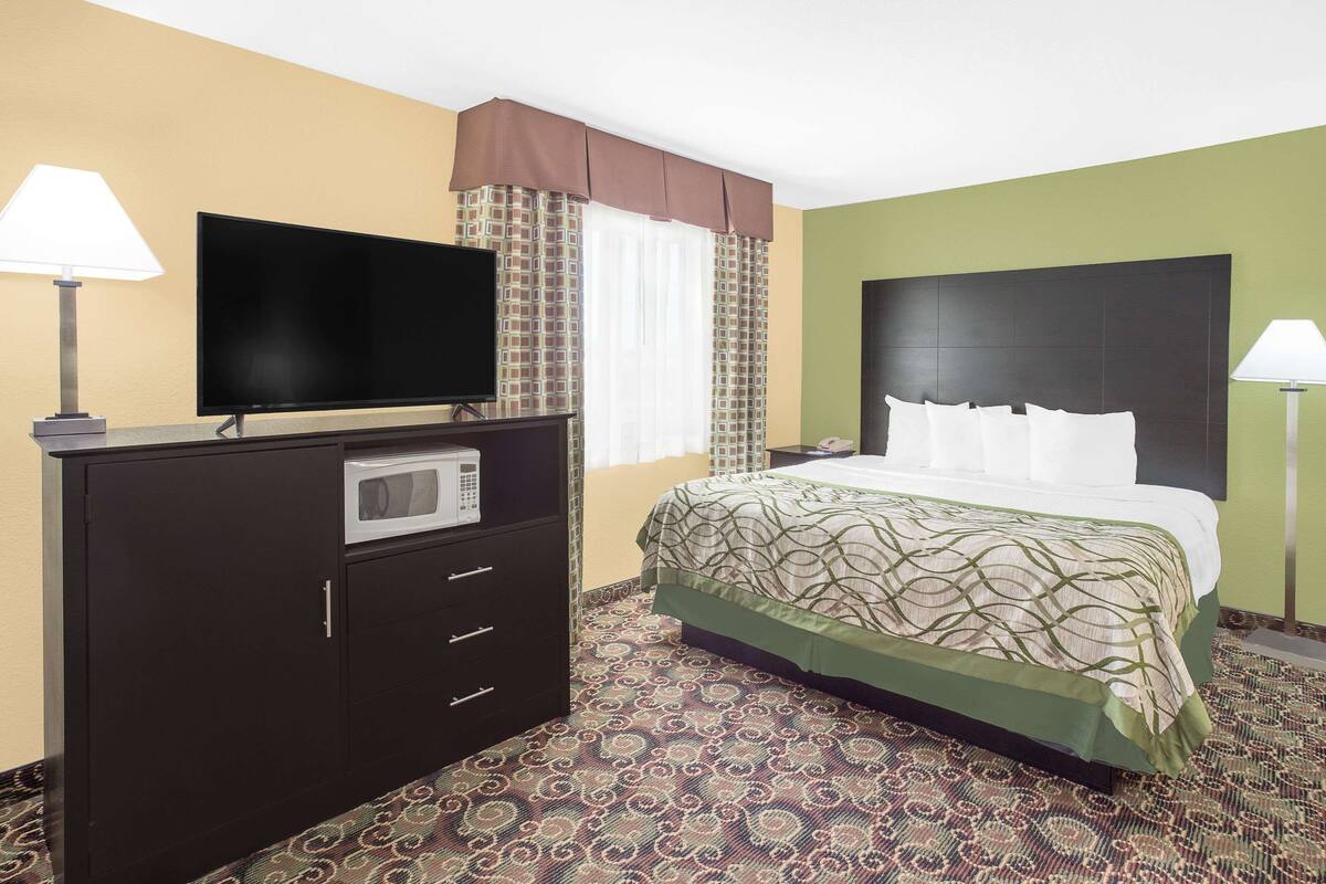 Une chambre d’hôtel avec un lit, un téléviseur posé sur une commode, un four à micro-ondes et une fenêtre avec des rideaux.