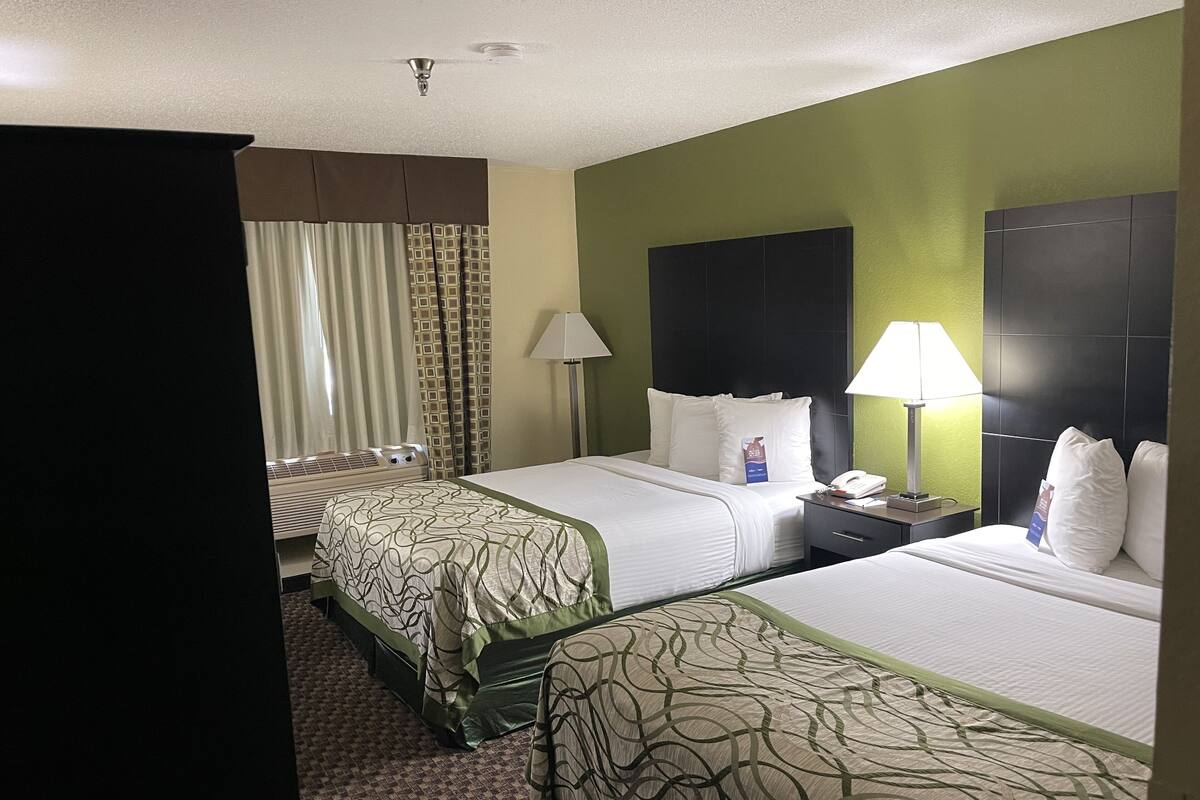 Une chambre d’hôtel avec deux lits, un bureau, une lampe et une fenêtre avec des rideaux.
