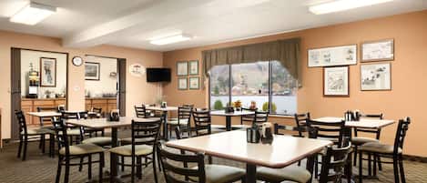 A dining area with multiple tables and chairs, a clock, framed pictures, and a view of a lake through large windows.