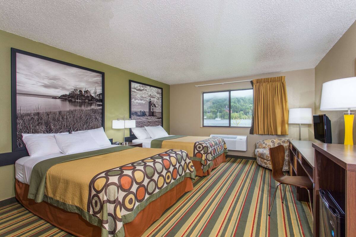 Een hotelkamer met twee bedden, een bureau, een stoel, een televisie en een raam met gordijnen.
