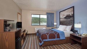A hotel room with a bed, a desk, a chair, a TV, a coffee maker, and a window with a view of a lake and trees.