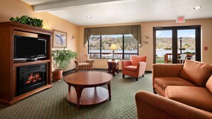 A hotel lobby with a fireplace, television, comfortable seating, a large window with a view, and an exit sign.