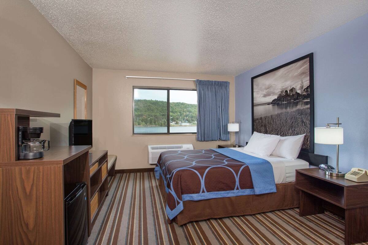 Een hotelkamer met een bed, een bureau, een koffiezetapparaat, een televisie, een raam met uitzicht op een meer en een schilderij aan de muur.