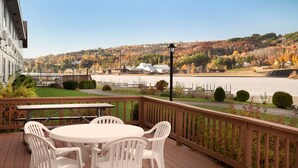 A deck with a table and chairs, overlooking a river and autumn-colored trees.