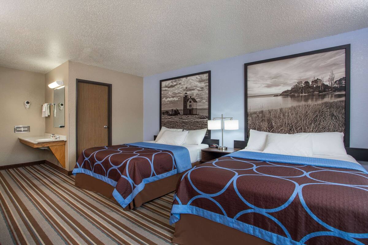 Een hotelkamer met twee bedden, een badkamer en twee grote landschapsprenten aan de muur.