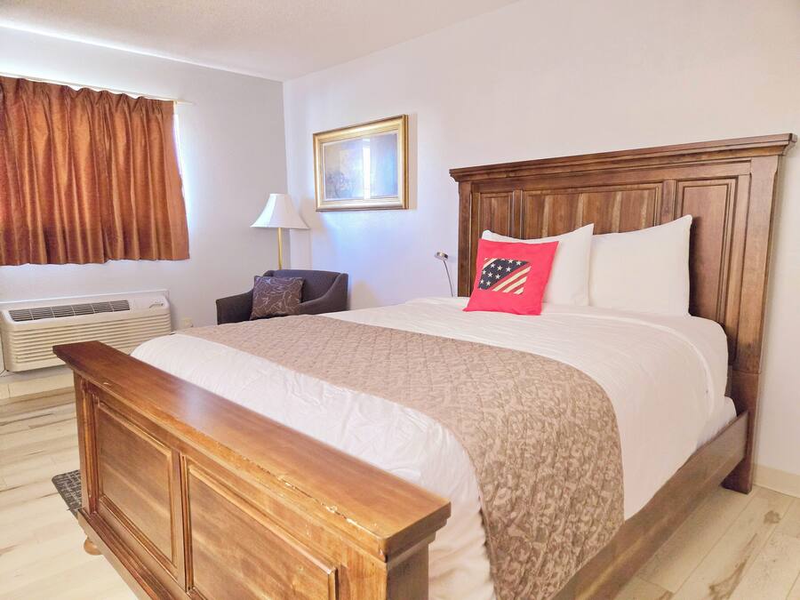 A hotel room with a large bed, a wooden bench, a desk, a chair, a lamp, and a framed picture on the wall.