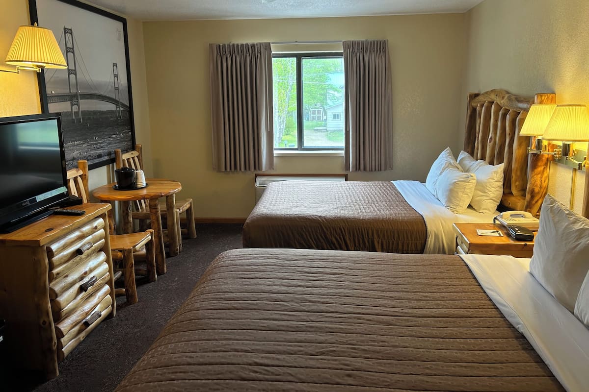 Une chambre d’hôtel avec un lit, un bureau avec une lampe, une télévision et une fenêtre avec des rideaux.