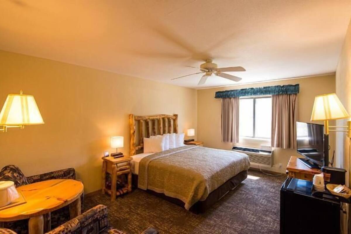 Une chambre d’hôtel comprenant un lit, un bureau avec une chaise, une télévision, un ventilateur de plafond et une fenêtre avec des rideaux.