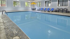 An indoor swimming pool with a stone floor, blue lounge chairs, and a yellow umbrella.