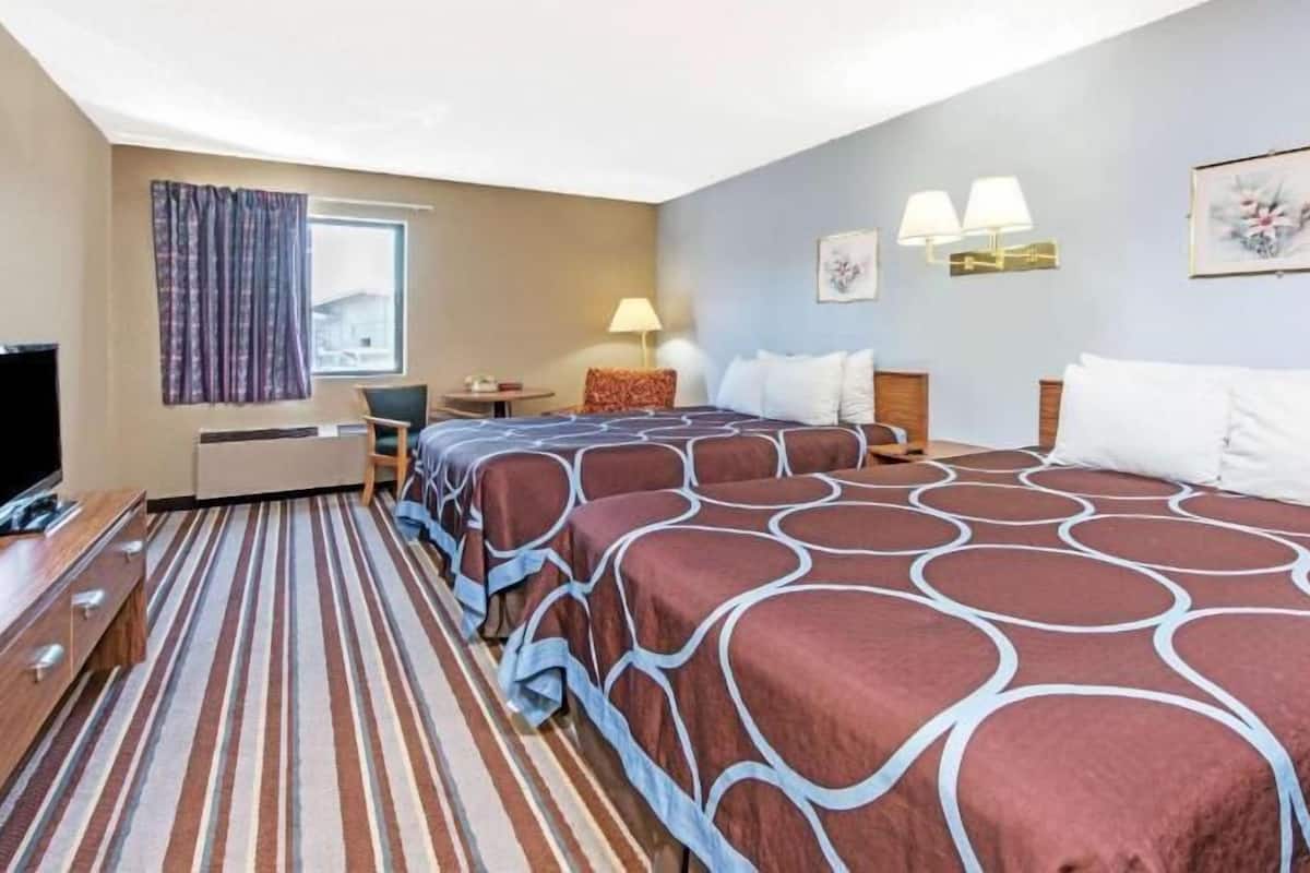 A hotel room with a bed, a desk, a TV, a lamp, and a window with curtains.