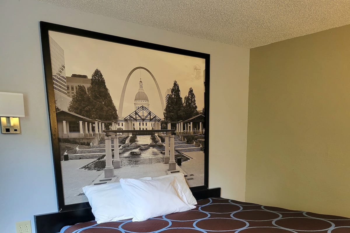A hotel room with a large bed, a nightstand with a remote control, and a framed picture of a cityscape on the wall.