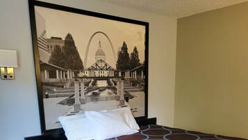 A hotel room with a large bed, a nightstand with a remote control, and a framed picture of a cityscape on the wall.