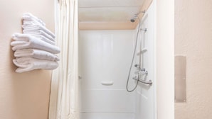 A shower area with a white bathtub, a towel rack with folded towels, and a showerhead. - Super 8 by Wyndham Sullivan (Sullivan)