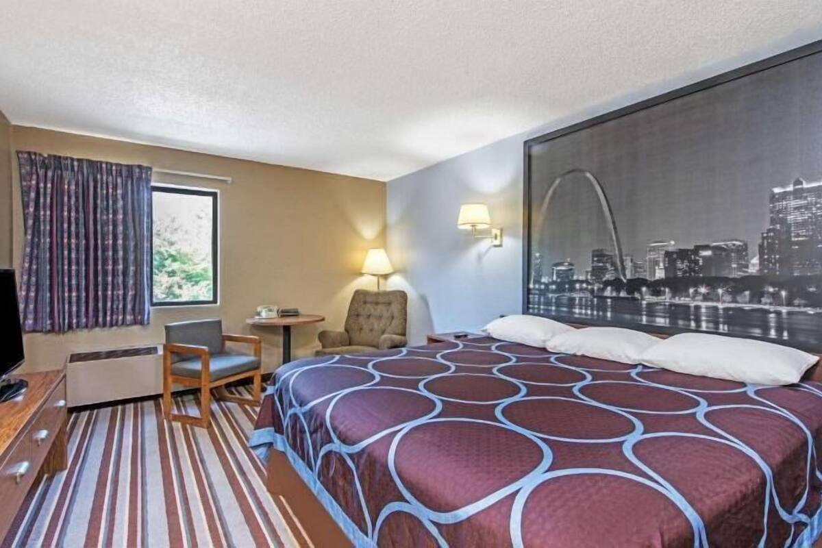 A hotel room with a bed, a desk, a chair, a TV, and a cityscape view.