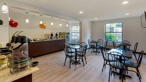 A modern kitchen with a coffee machine, a refrigerator, and a dining area with chairs and tables. - Quality Inn Lee - Lenox South (Lee)