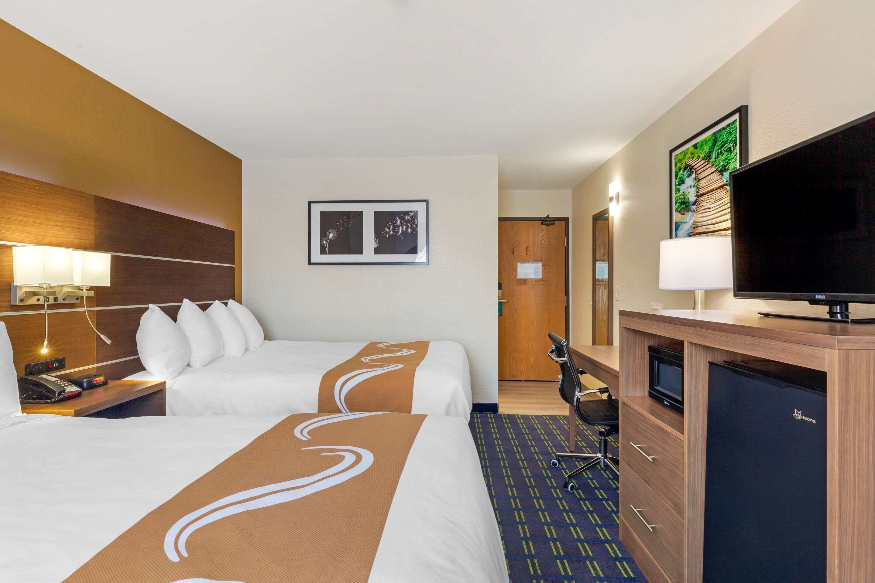 A hotel room with two beds, a desk with a computer, a TV, and a minibar.