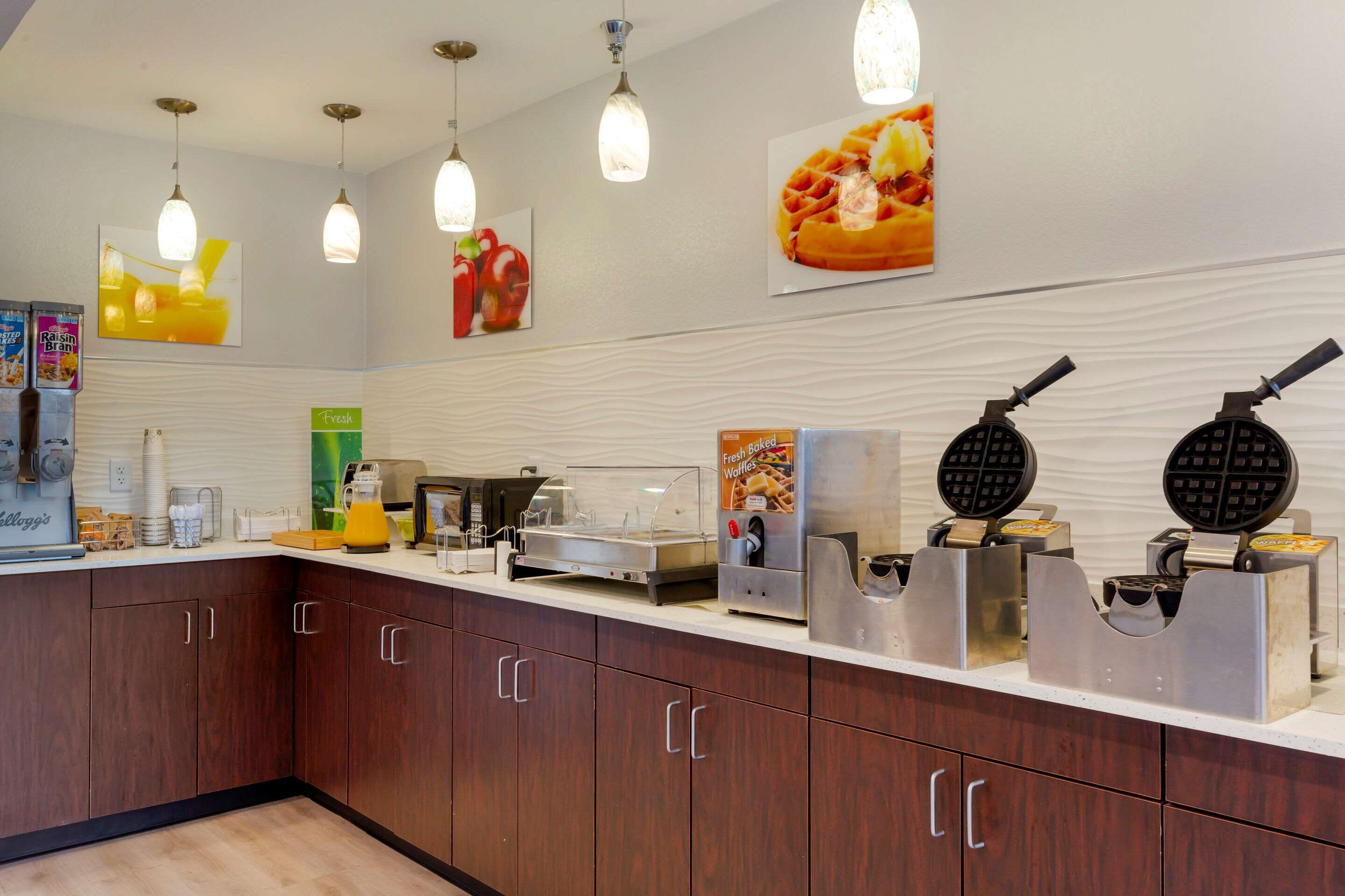 A kitchen area with waffle makers, a coffee machine, and a fresh juice dispenser.